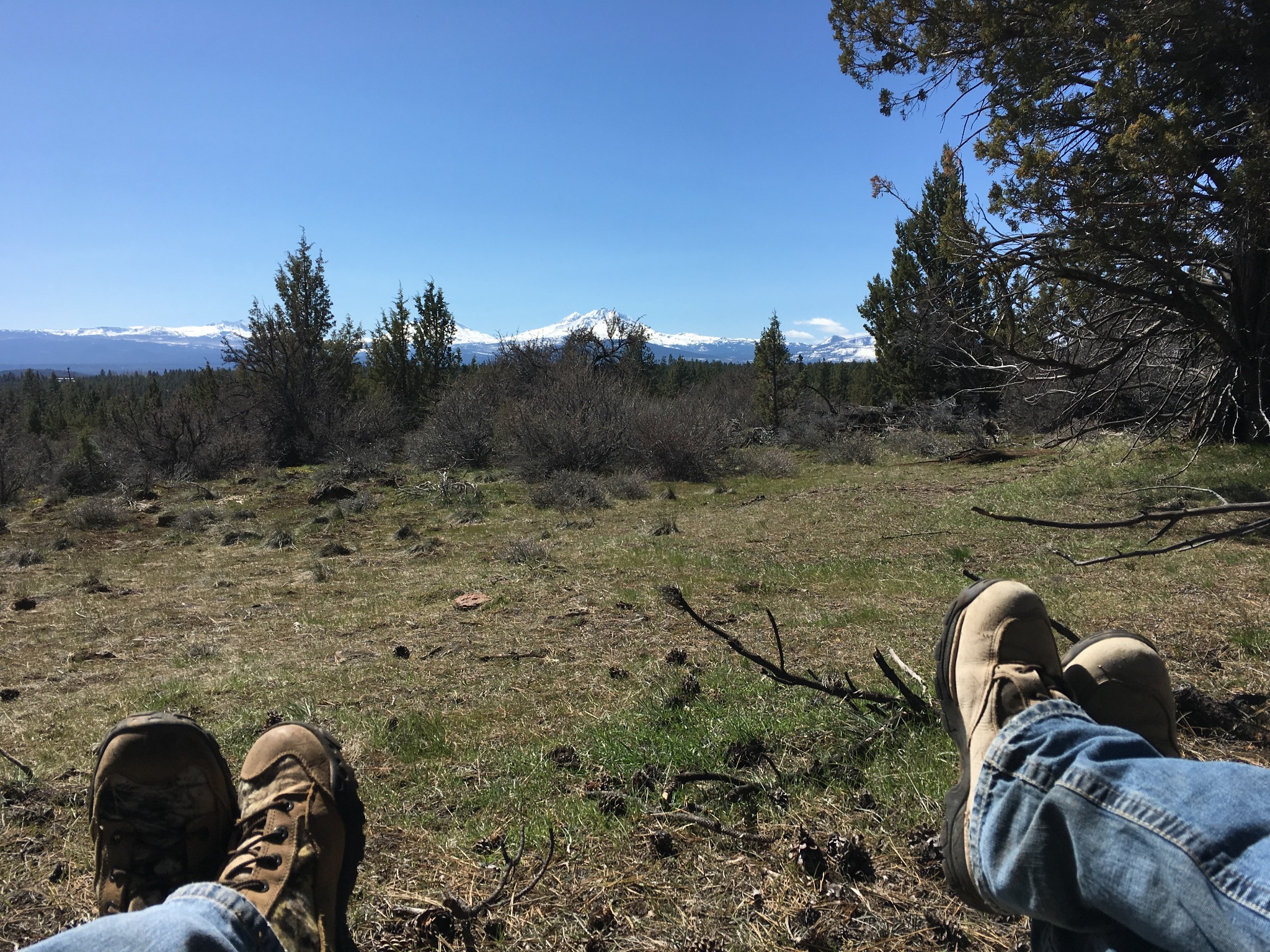 Boots resting in the foreground, looking across a Central Oregon landscape toward the snow-capped Cascades.